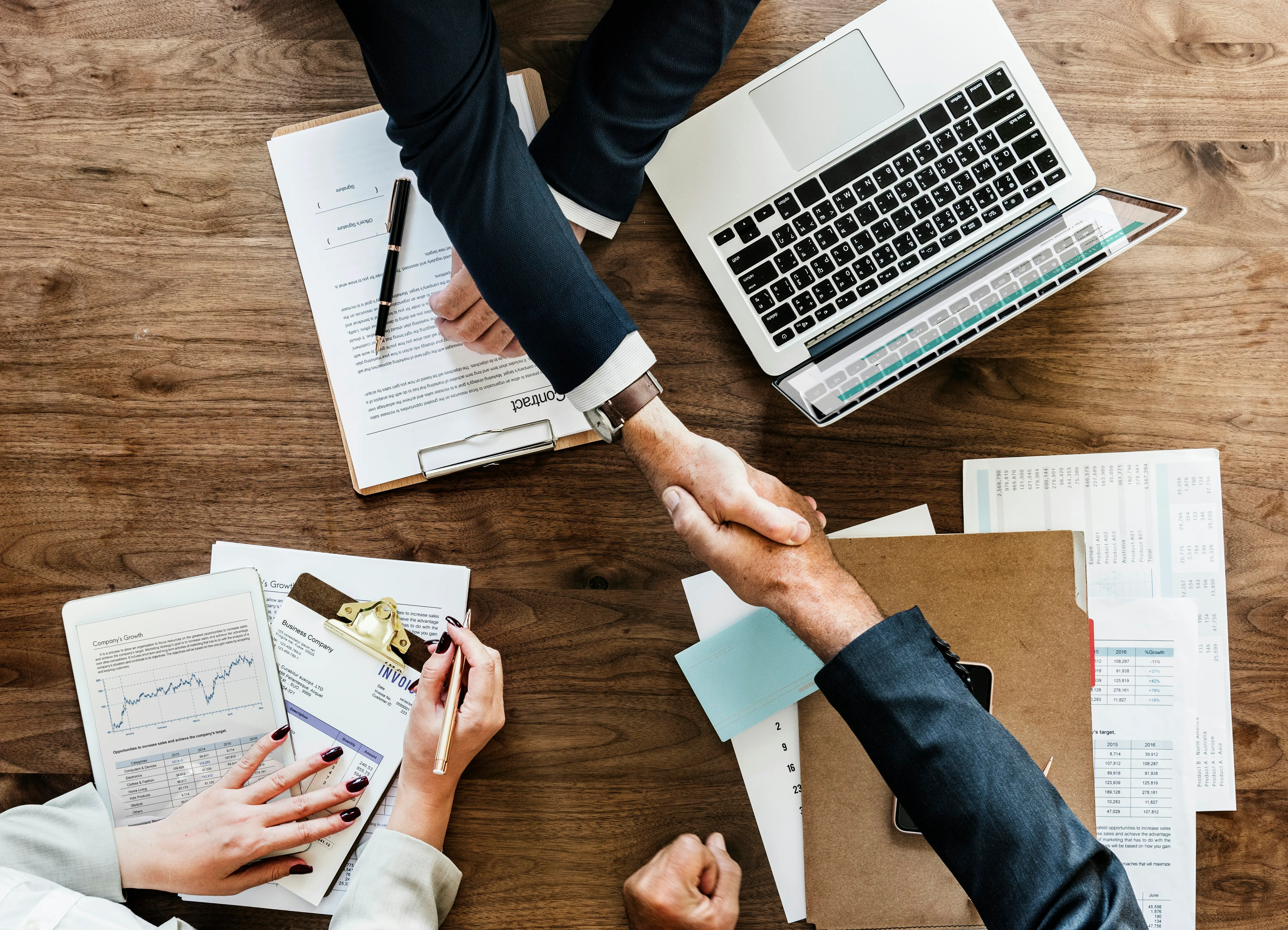 two people handshaking above table with laptop